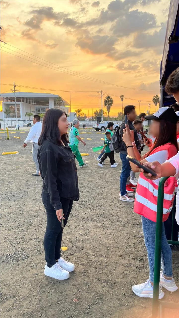 Foto en exteriores de una mujer sosteniendo un teléfono hacia personas en la entrada de un evento.