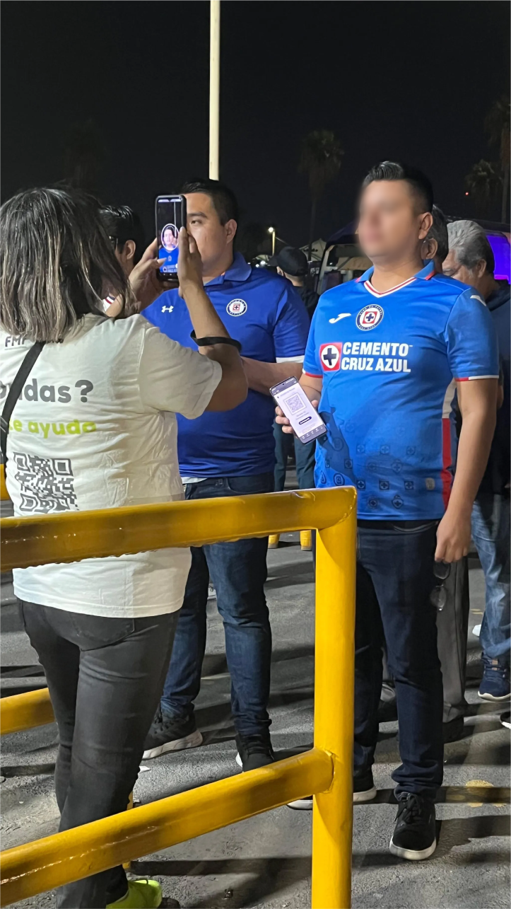 Foto nocturna de un evento con personal en camisas azules asistiendo a los asistentes en un mostrador.