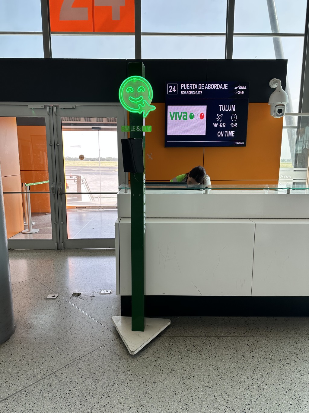 Kiosco verde de autoservicio de Fan ID frente a un mostrador de registro del aeropuerto.