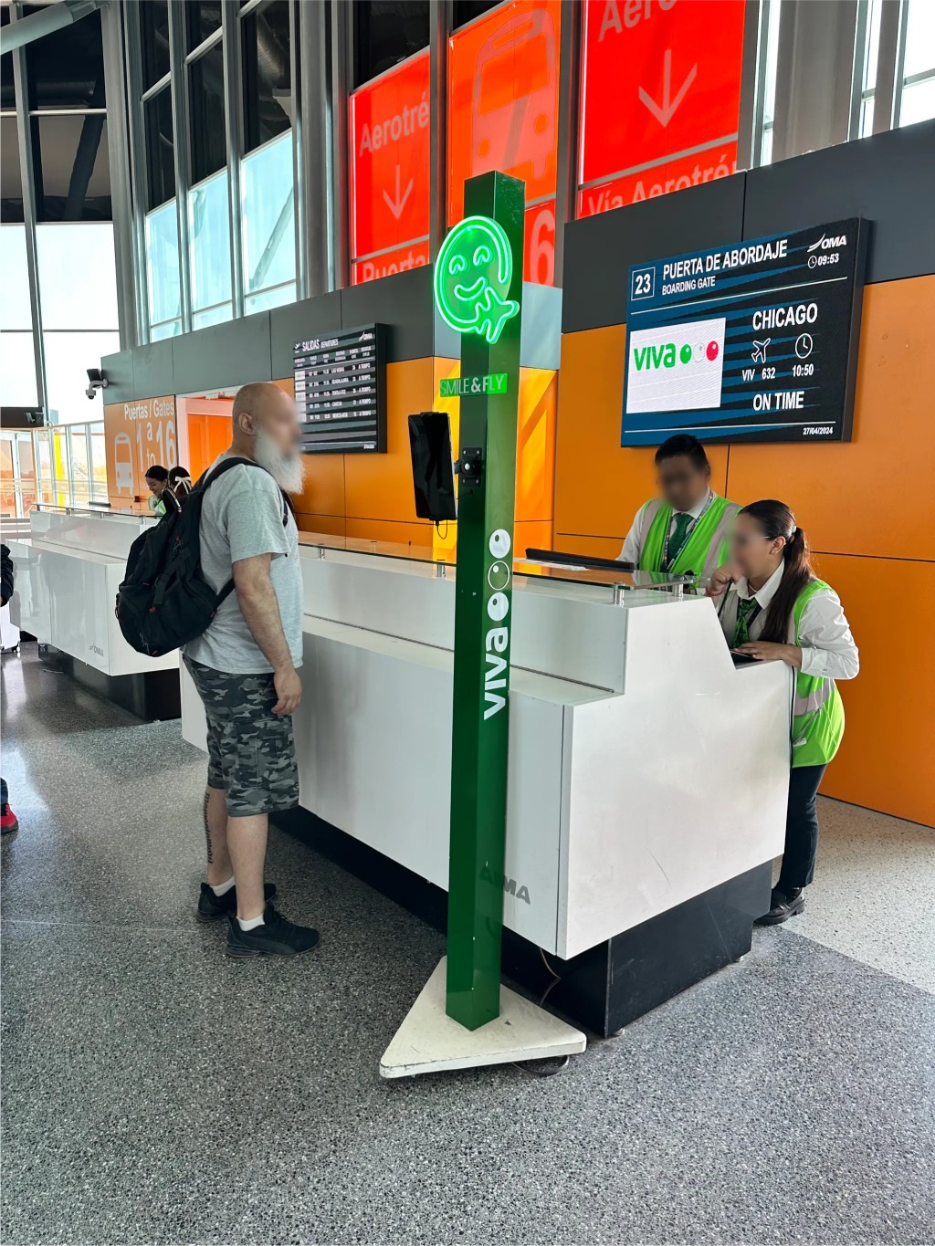 Área de registro de aeropuerto con un kiosco verde de Fan ID junto a un mostrador de servicio.