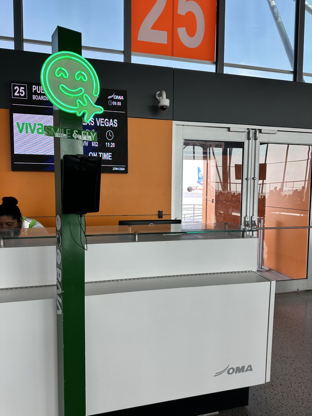 Kiosco verde de Fan ID junto a un mostrador de aeropuerto marcado con el número 23.